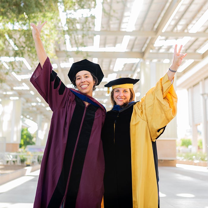 Graduates in commencement robes embracing and celebrating at Tempe campus